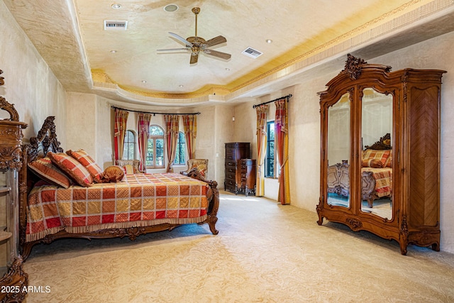 bedroom featuring light carpet, a tray ceiling, crown molding, and ceiling fan