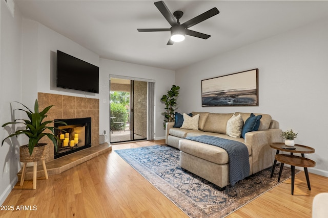 living area with wood finished floors, baseboards, a tile fireplace, and a ceiling fan