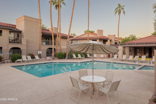 pool at dusk featuring a patio area, a community pool, and fence