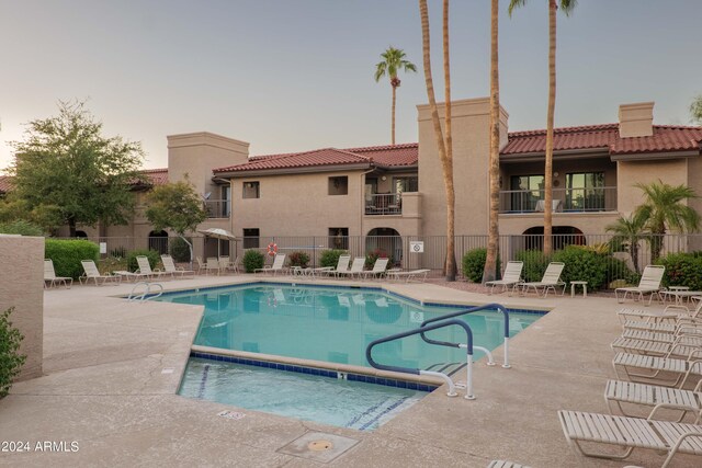 pool at dusk with fence, a community pool, and a patio area