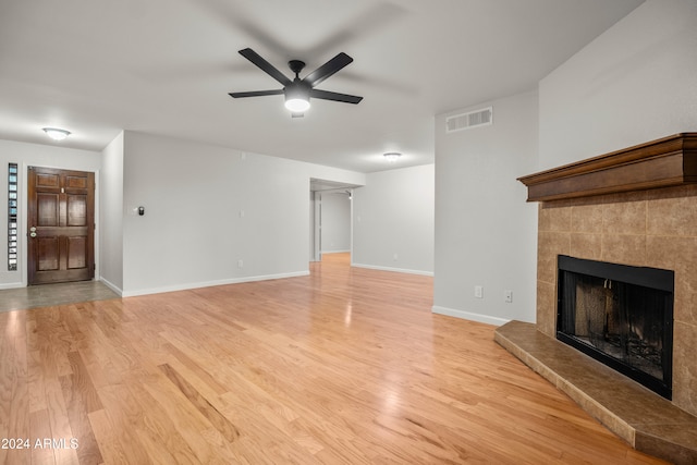 unfurnished living room with ceiling fan, light wood-type flooring, and a tiled fireplace