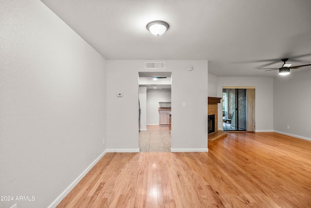 unfurnished room with a tile fireplace, light hardwood / wood-style flooring, and ceiling fan