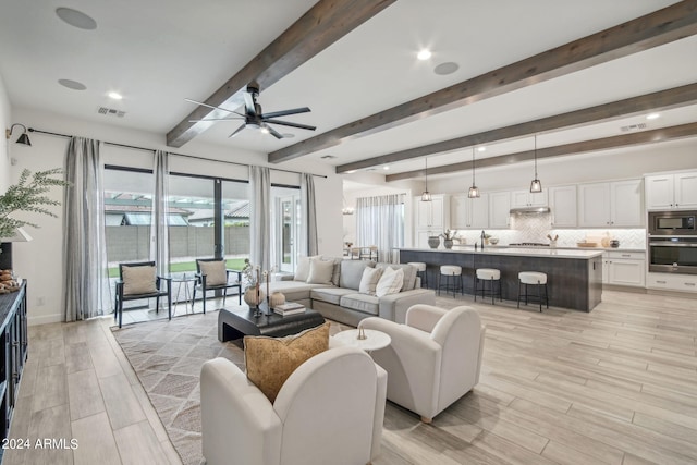 living area with a ceiling fan, light wood-style flooring, visible vents, and beamed ceiling