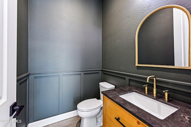 half bath featuring a textured wall, toilet, wainscoting, vanity, and wood finished floors