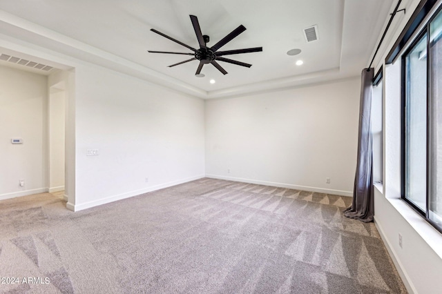 empty room featuring a raised ceiling, visible vents, plenty of natural light, and baseboards