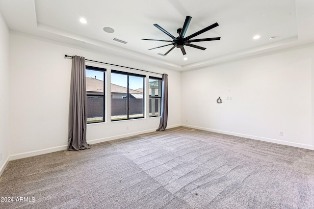 carpeted spare room featuring a tray ceiling, visible vents, and baseboards