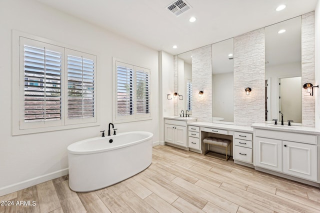 bathroom featuring a freestanding tub, visible vents, a sink, and wood finished floors