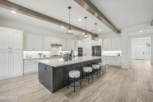 kitchen featuring stainless steel appliances, wood tiled floor, white cabinetry, and a large island with sink