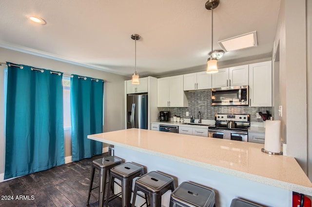 kitchen with pendant lighting, dark hardwood / wood-style flooring, a kitchen bar, white cabinetry, and stainless steel appliances