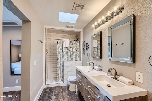 bathroom featuring hardwood / wood-style floors, vanity, a skylight, toilet, and walk in shower