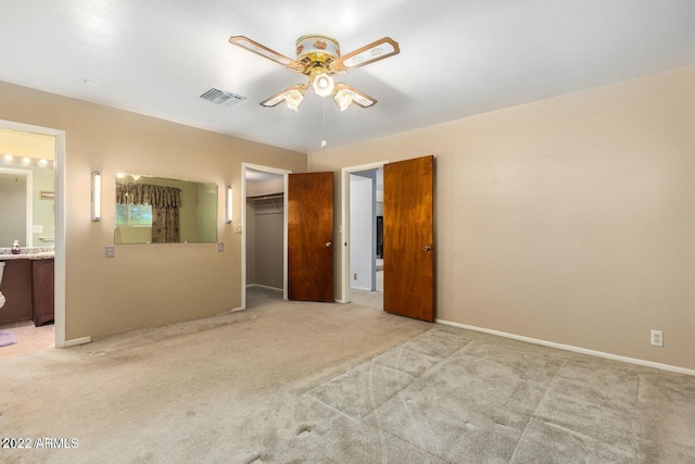 unfurnished bedroom with light carpet, a closet, ensuite bathroom, and ceiling fan