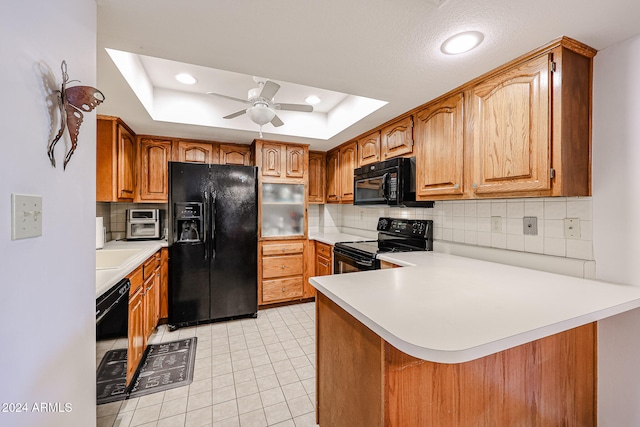 kitchen with ceiling fan, a raised ceiling, kitchen peninsula, decorative backsplash, and black appliances