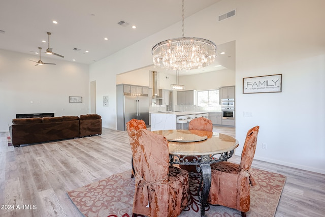 dining space featuring light hardwood / wood-style flooring, ceiling fan with notable chandelier, and a high ceiling