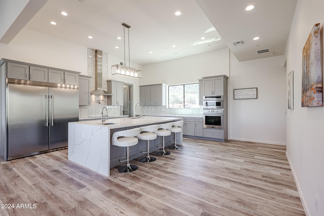 kitchen featuring a kitchen island with sink, light hardwood / wood-style flooring, stainless steel appliances, and wall chimney range hood