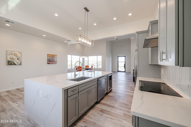 kitchen featuring gray cabinetry, light stone counters, dishwasher, and an island with sink