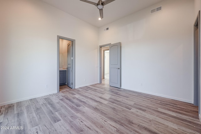 unfurnished bedroom featuring ensuite bath, ceiling fan, a towering ceiling, and light wood-type flooring