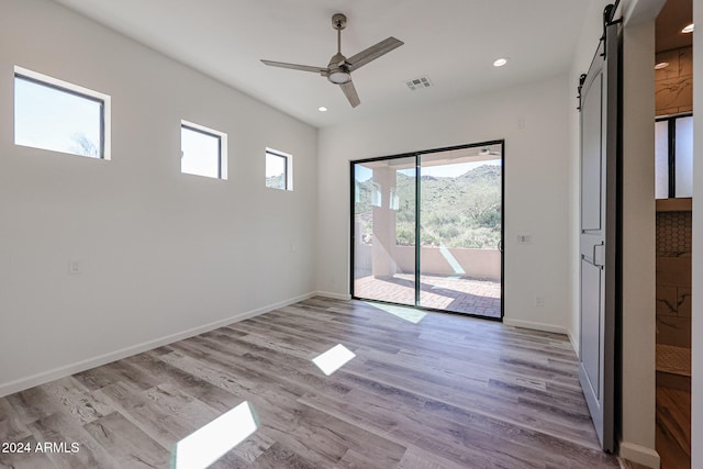 spare room featuring a barn door, ceiling fan, and light hardwood / wood-style floors