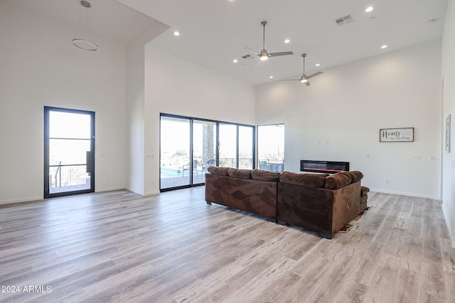 living room with ceiling fan, light hardwood / wood-style floors, a towering ceiling, and a wealth of natural light