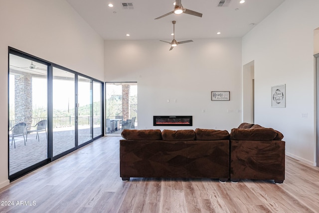 living room featuring ceiling fan, a high ceiling, and light wood-type flooring