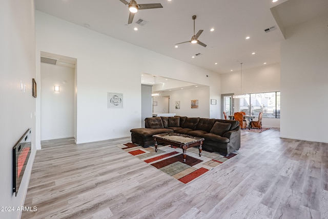 living room with ceiling fan, light hardwood / wood-style flooring, and a high ceiling