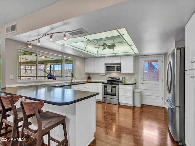 kitchen featuring stainless steel appliances, dark countertops, visible vents, white cabinetry, and a peninsula