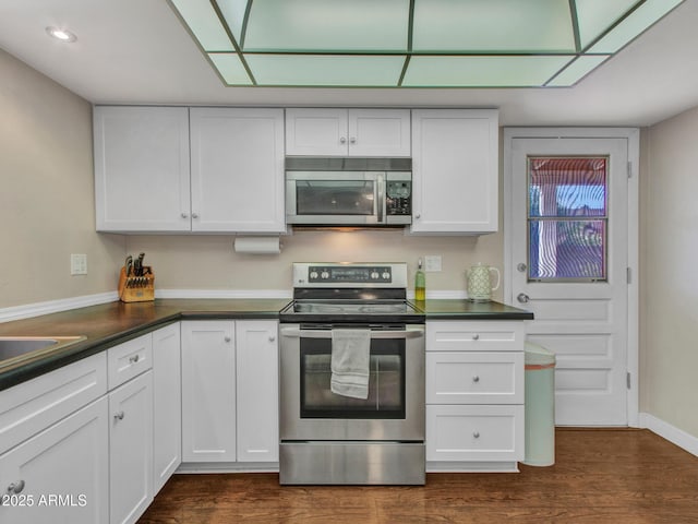 kitchen featuring baseboards, white cabinets, dark wood finished floors, dark countertops, and stainless steel appliances