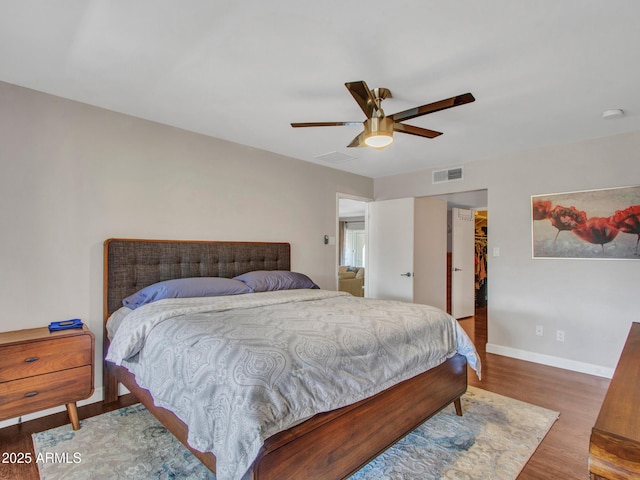 bedroom featuring a walk in closet, visible vents, ceiling fan, wood finished floors, and baseboards