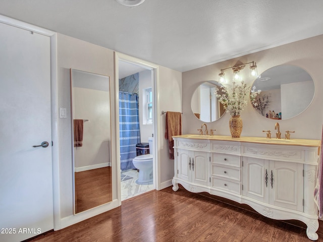 bathroom with double vanity, toilet, a sink, and wood finished floors