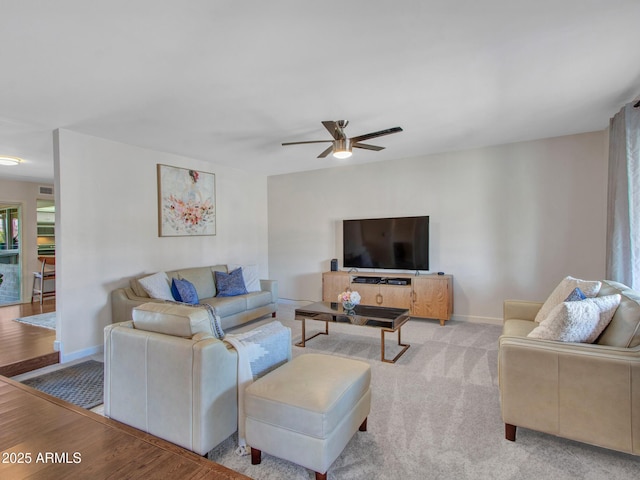 living area with light carpet, light wood-type flooring, a ceiling fan, and baseboards