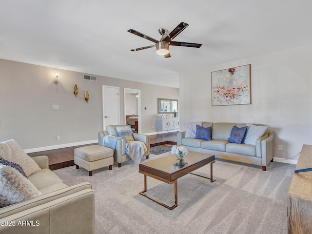 living room featuring baseboards, visible vents, a ceiling fan, and light colored carpet