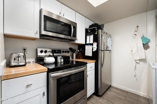 kitchen with appliances with stainless steel finishes, wood counters, light hardwood / wood-style floors, and white cabinets