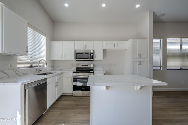 kitchen featuring light stone countertops, appliances with stainless steel finishes, sink, white cabinets, and a kitchen island