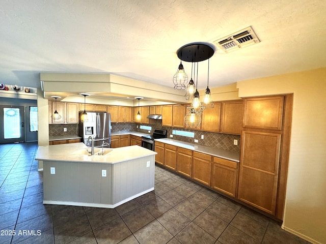 kitchen featuring stainless steel appliances, pendant lighting, light countertops, and a center island with sink