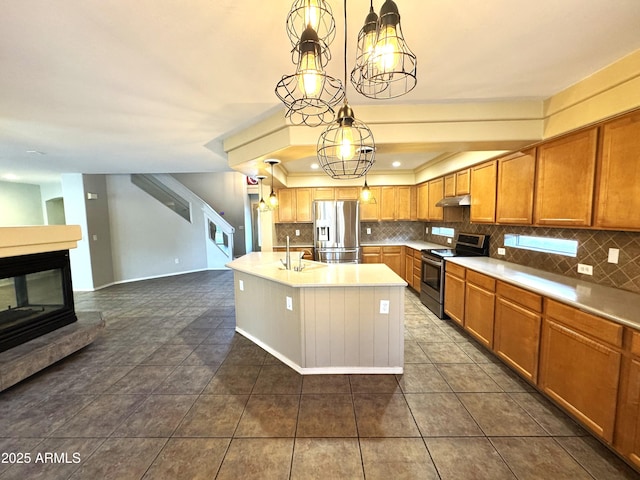 kitchen featuring decorative light fixtures, a kitchen island with sink, stainless steel appliances, light countertops, and under cabinet range hood