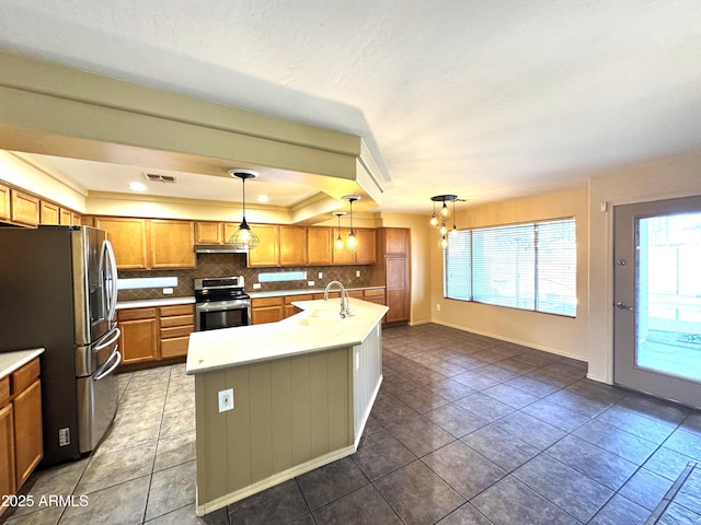 kitchen with stainless steel appliances, a sink, hanging light fixtures, light countertops, and an island with sink