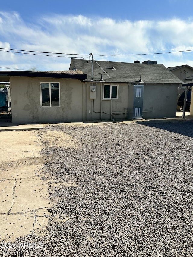 back of property with a shingled roof and stucco siding