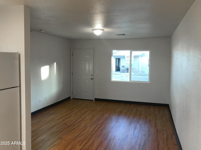 unfurnished room with visible vents, dark wood finished floors, a textured ceiling, and baseboards