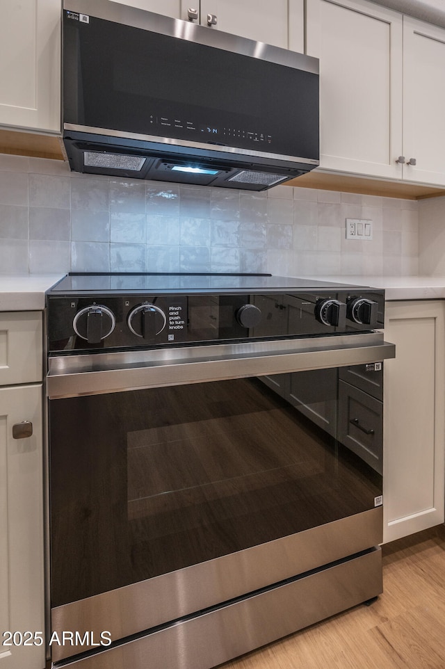 866 W Geronimo St, Chandler, AZ 85225 - kitchen view of stainless steel electric range oven, range hood, light countertops, white cabinets, and tasteful backsplash