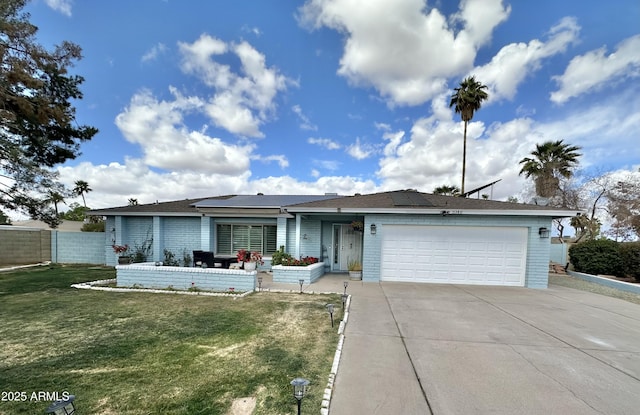 ranch-style home featuring concrete driveway, an attached garage, fence, roof mounted solar panels, and a front yard