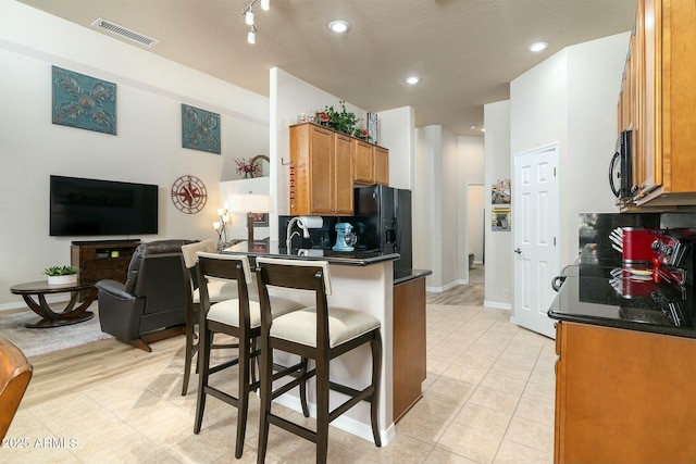 kitchen featuring a breakfast bar, black appliances, sink, light tile patterned floors, and kitchen peninsula