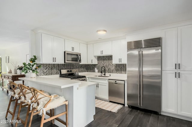 kitchen with light countertops, appliances with stainless steel finishes, white cabinets, a sink, and a peninsula