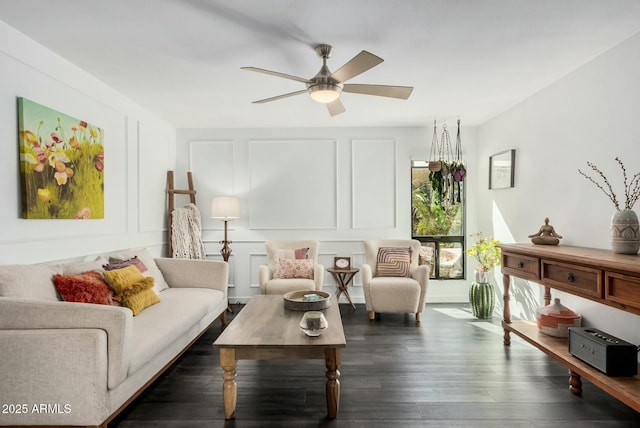 living area featuring ceiling fan, a decorative wall, and dark wood-style flooring