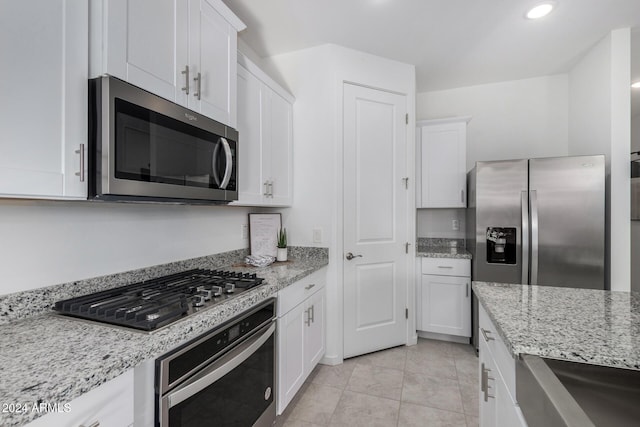 kitchen featuring white cabinets, light tile patterned floors, light stone countertops, and appliances with stainless steel finishes