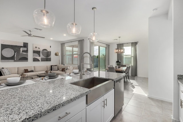 kitchen featuring white cabinets, hanging light fixtures, stainless steel dishwasher, light tile patterned floors, and light stone counters