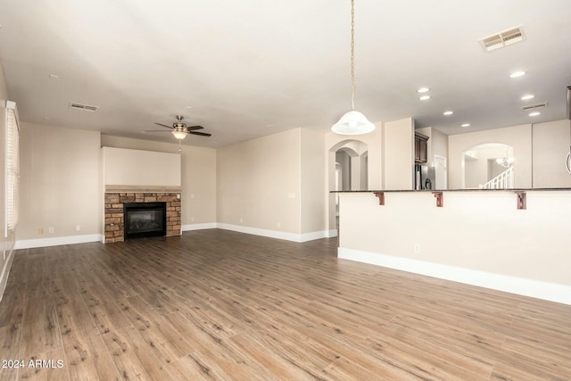 unfurnished living room featuring a stone fireplace, ceiling fan, and hardwood / wood-style floors