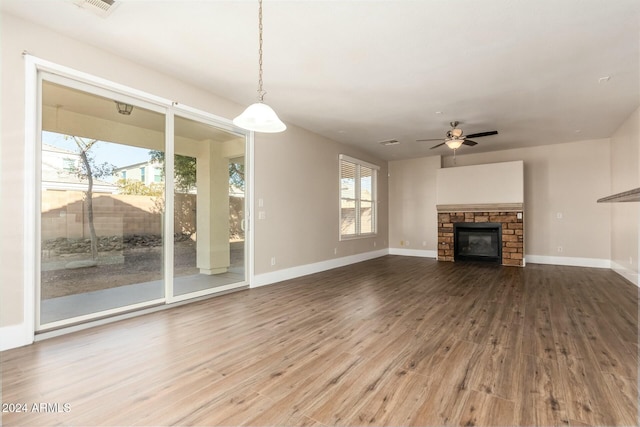 unfurnished living room with hardwood / wood-style flooring, ceiling fan, a stone fireplace, and a wealth of natural light