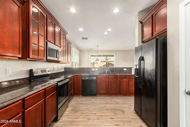 kitchen with light wood-type flooring, sink, black appliances, dark stone countertops, and hanging light fixtures