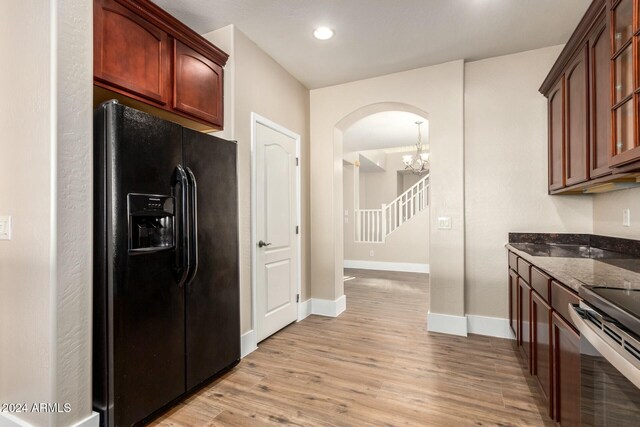 kitchen with dark stone counters, an inviting chandelier, black fridge, electric stove, and light hardwood / wood-style flooring