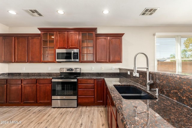 kitchen with appliances with stainless steel finishes, light hardwood / wood-style flooring, dark stone counters, and sink