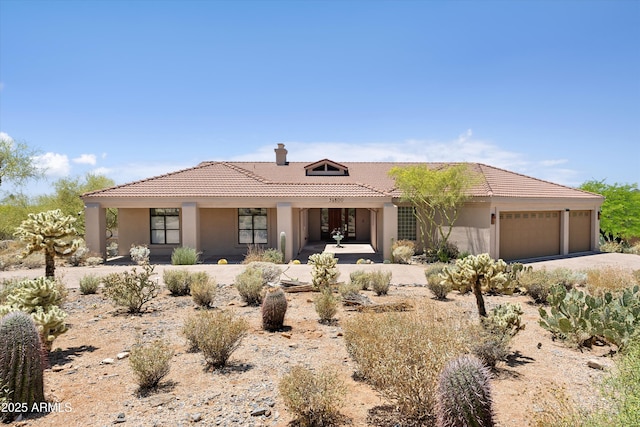 view of front facade with stucco siding, a chimney, an attached garage, and a tiled roof